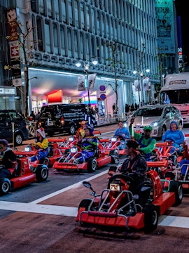 Tourists driving go-karts in Osaka dressed as Mario characters, cityscape in the background.