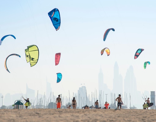 People enjoying water activities at Kite Beach, Dubai, with the iconic Burj Al Arab in the background.
