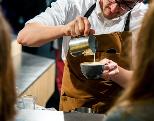 Barista pouring milk into coffee
