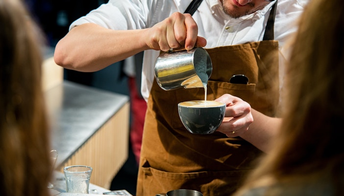 Barista pouring milk into coffee