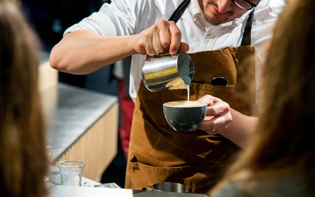 Barista pouring milk into coffee