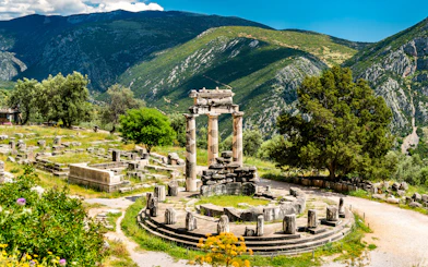 Visitors at the Temple of Apollo in Delphi, Greece, surrounded by ancient ruins and mountains.
