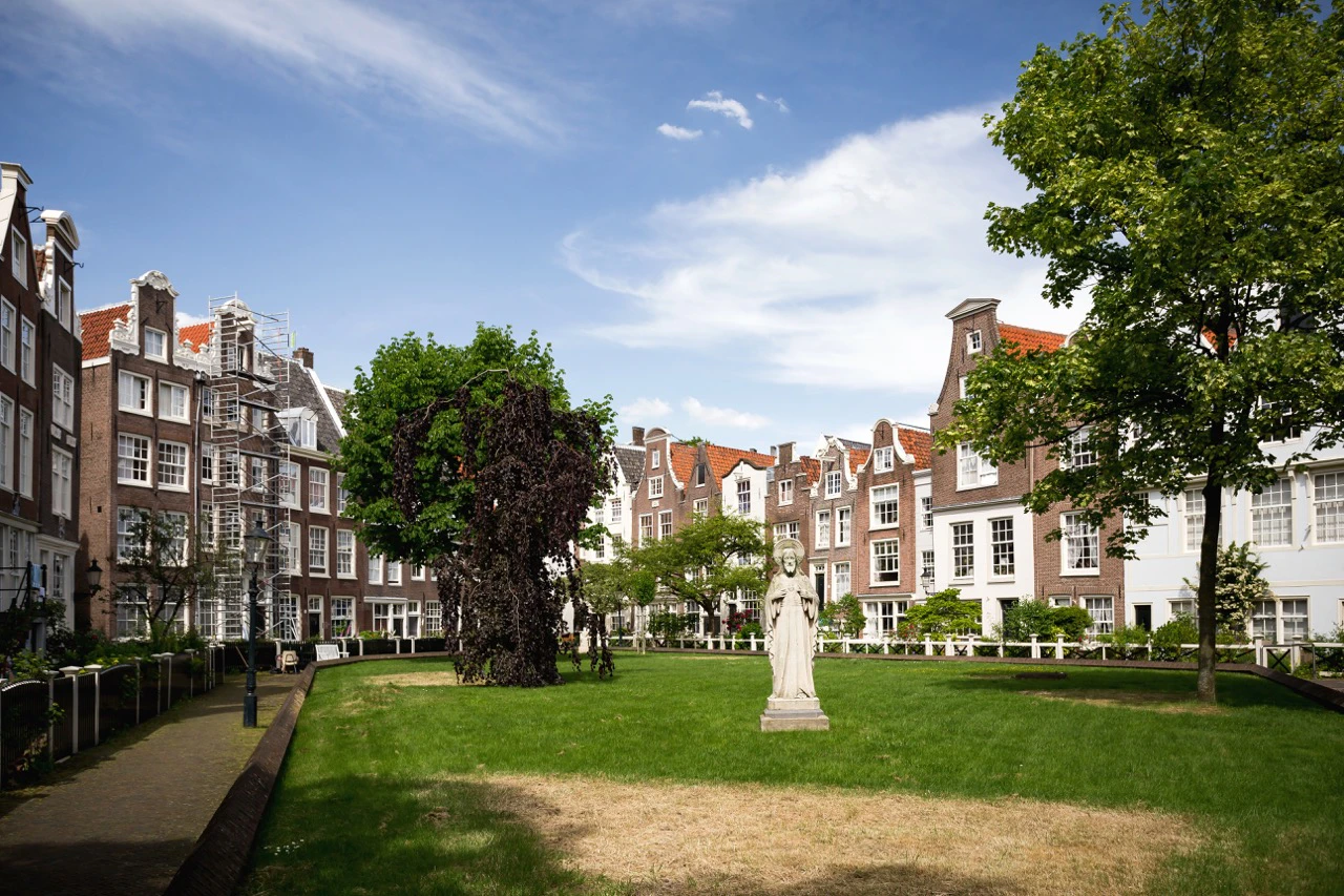 Amsterdam Begijnhof courtyard with historic buildings and a statue.