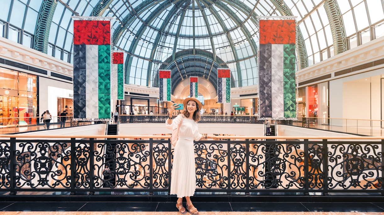 Woman taking a selfie inside Mall of the Emirates, Dubai, with UAE flags displayed.