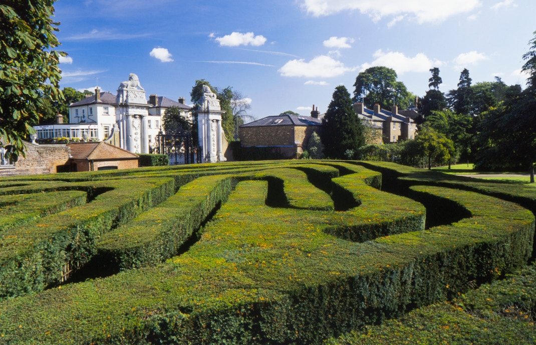 Hampton Court Palace garden maze with historic buildings in the background.