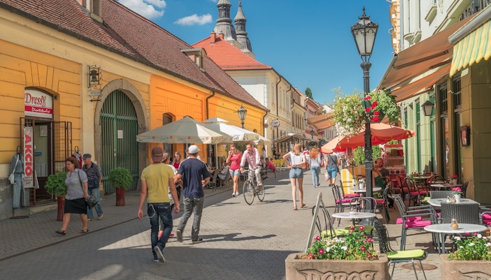 Pedestrian street with cafes and shops in Eger, Hungary, featuring people walking and cycling.