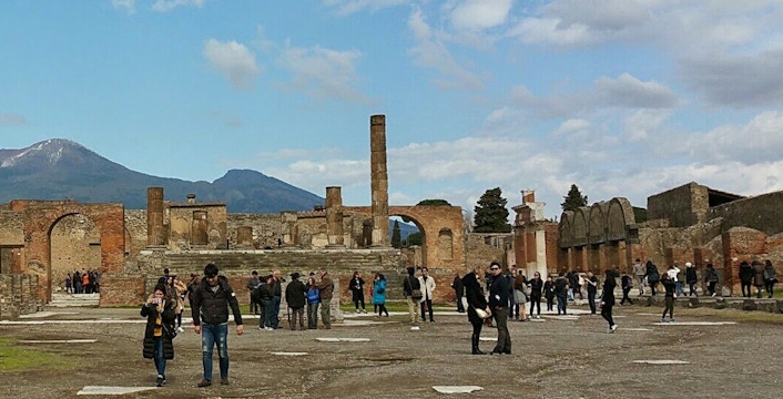 Visitors exploring ancient ruins with Mount Vesuvius in the background, Herculaneum Ruins Guided Tours.