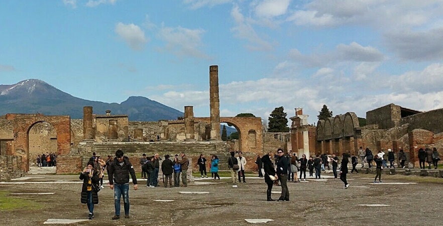 Visitors exploring ancient ruins with Mount Vesuvius in the background, Herculaneum Ruins Guided Tours.