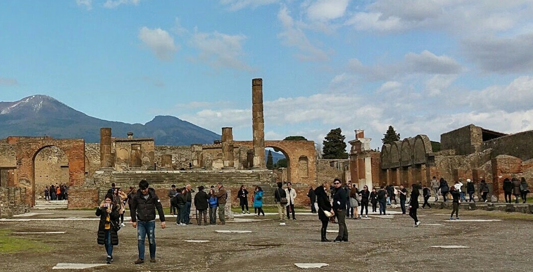 Visitors exploring ancient ruins with Mount Vesuvius in the background, Herculaneum Ruins Guided Tours.