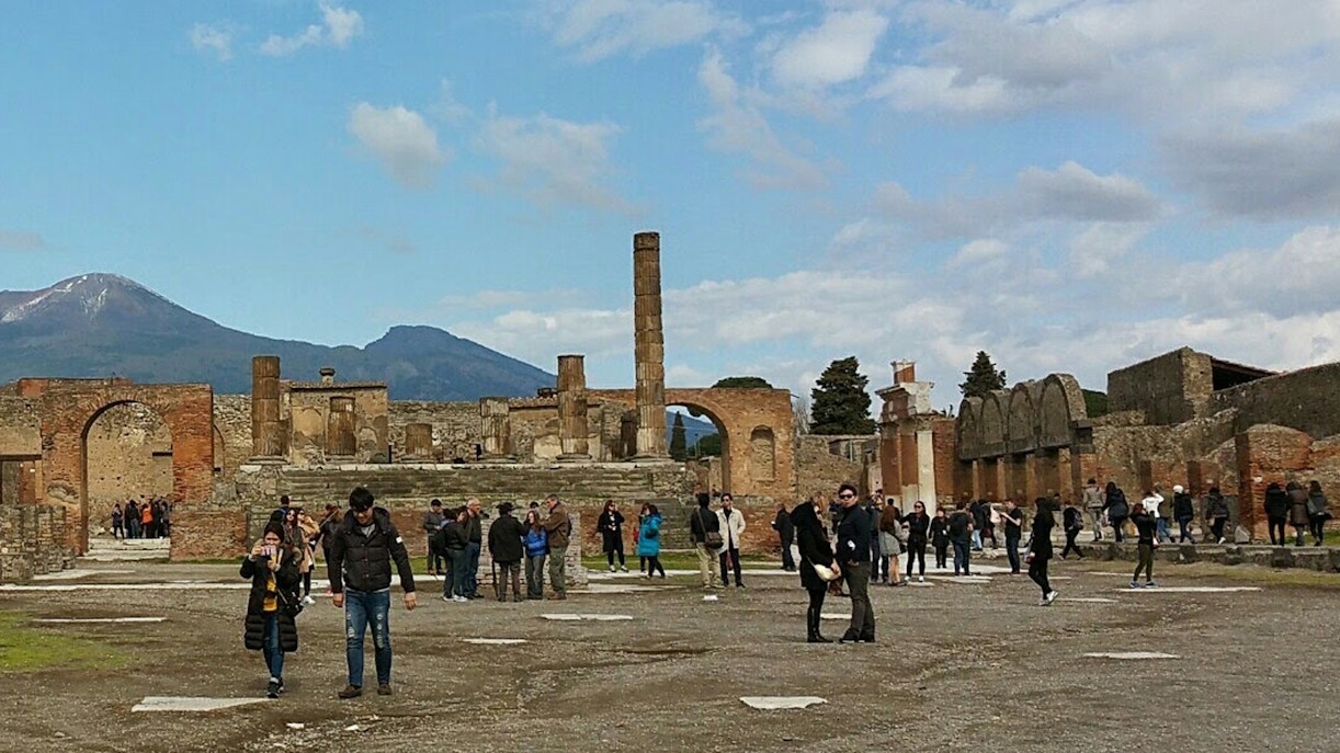 Visitors exploring ancient ruins with Mount Vesuvius in the background, Herculaneum Ruins Guided Tours.