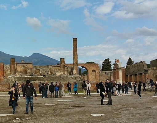 Visitors exploring ancient ruins with Mount Vesuvius in the background, Herculaneum Ruins Guided Tours.
