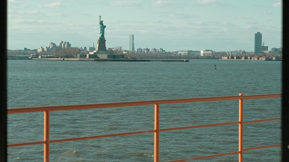 NYC ferry sailing past the Statue of Liberty with Manhattan skyline in the background.