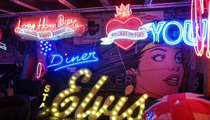 Neon signs at God's Own Junkyard in London, featuring "Elvis" and pop art mural.