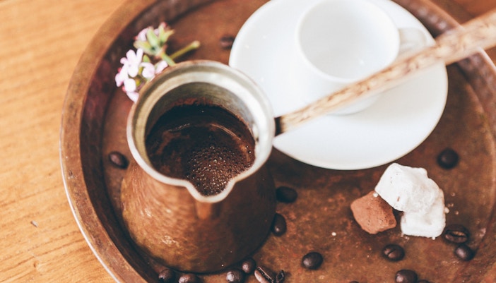 Greek coffee in a traditional pot with sugar cubes and an empty cup on a tray in Athens.