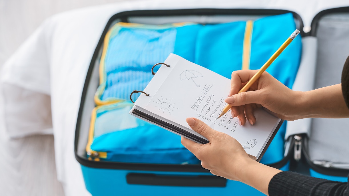 Open suitcase with packing cubes and a person checking a travel essentials list.