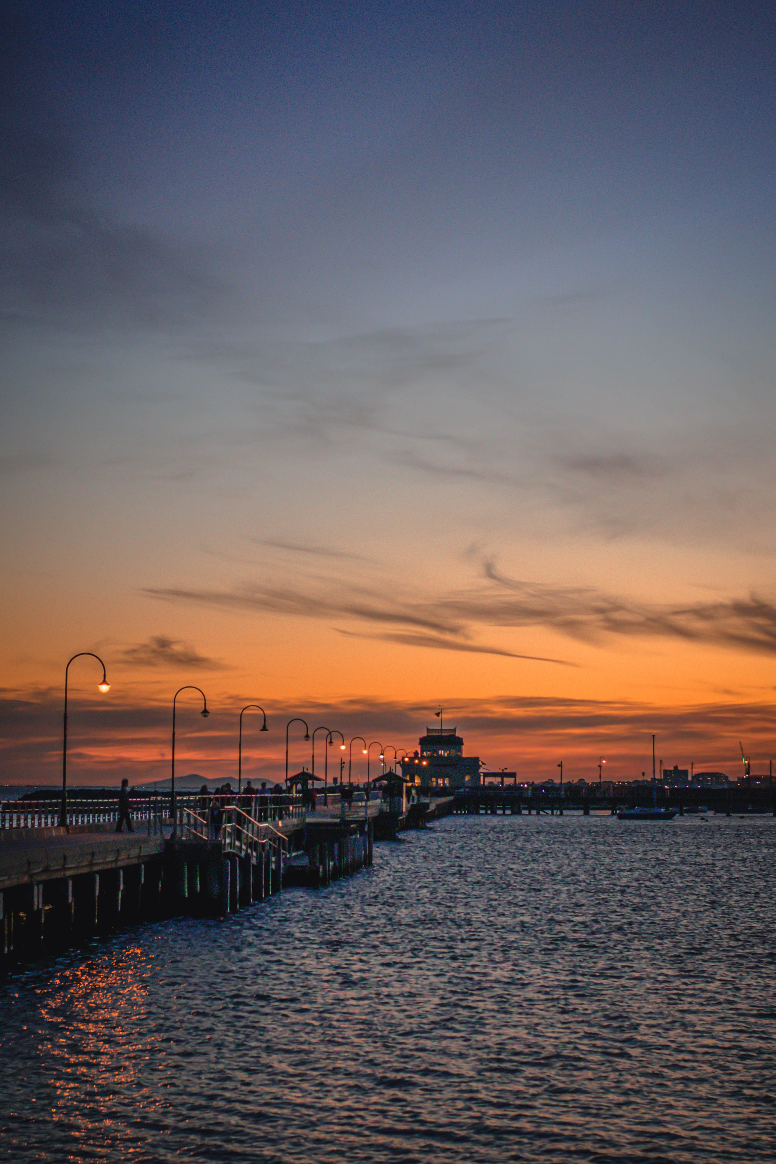 St. Kilda pier at sunset with silhouetted lampposts and calm water.