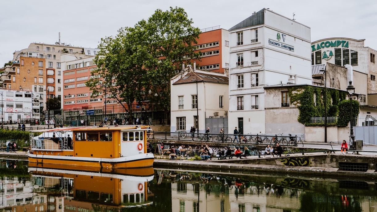 Canal Saint-Martin in Paris with a yellow boat and people relaxing by the water.