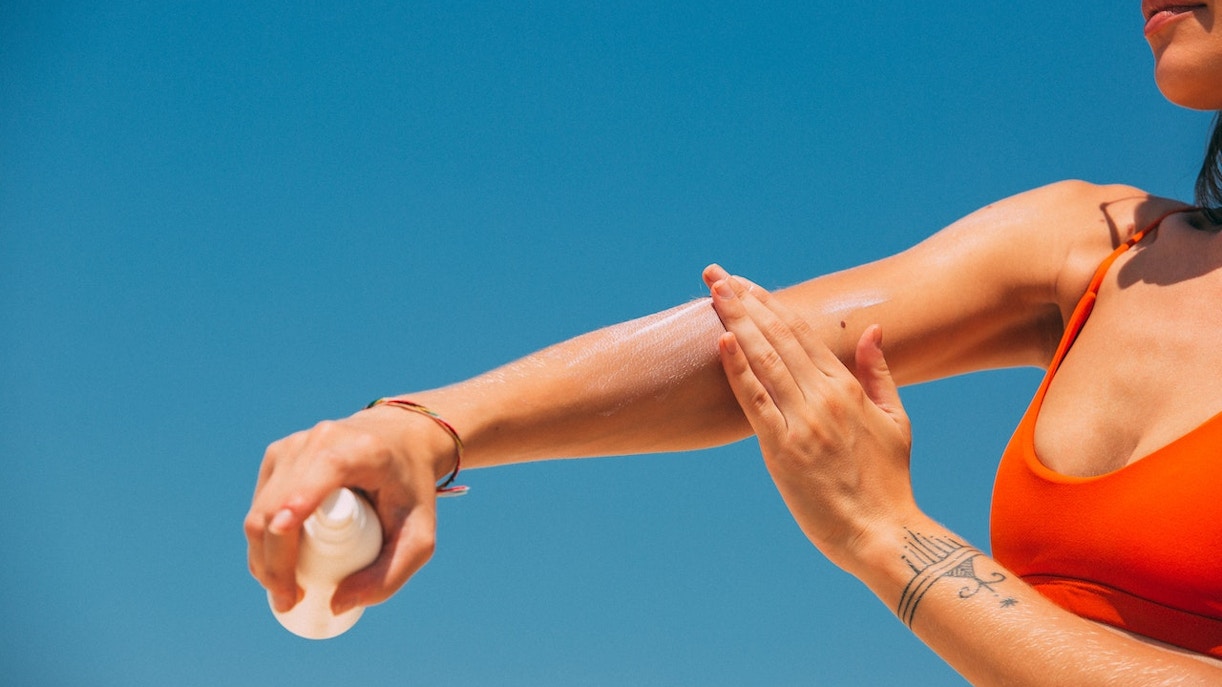 Applying sunscreen on arm under clear Sydney sky.