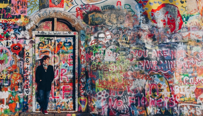 Person posing in front of vibrant grafitti art Lennon Wall Prague