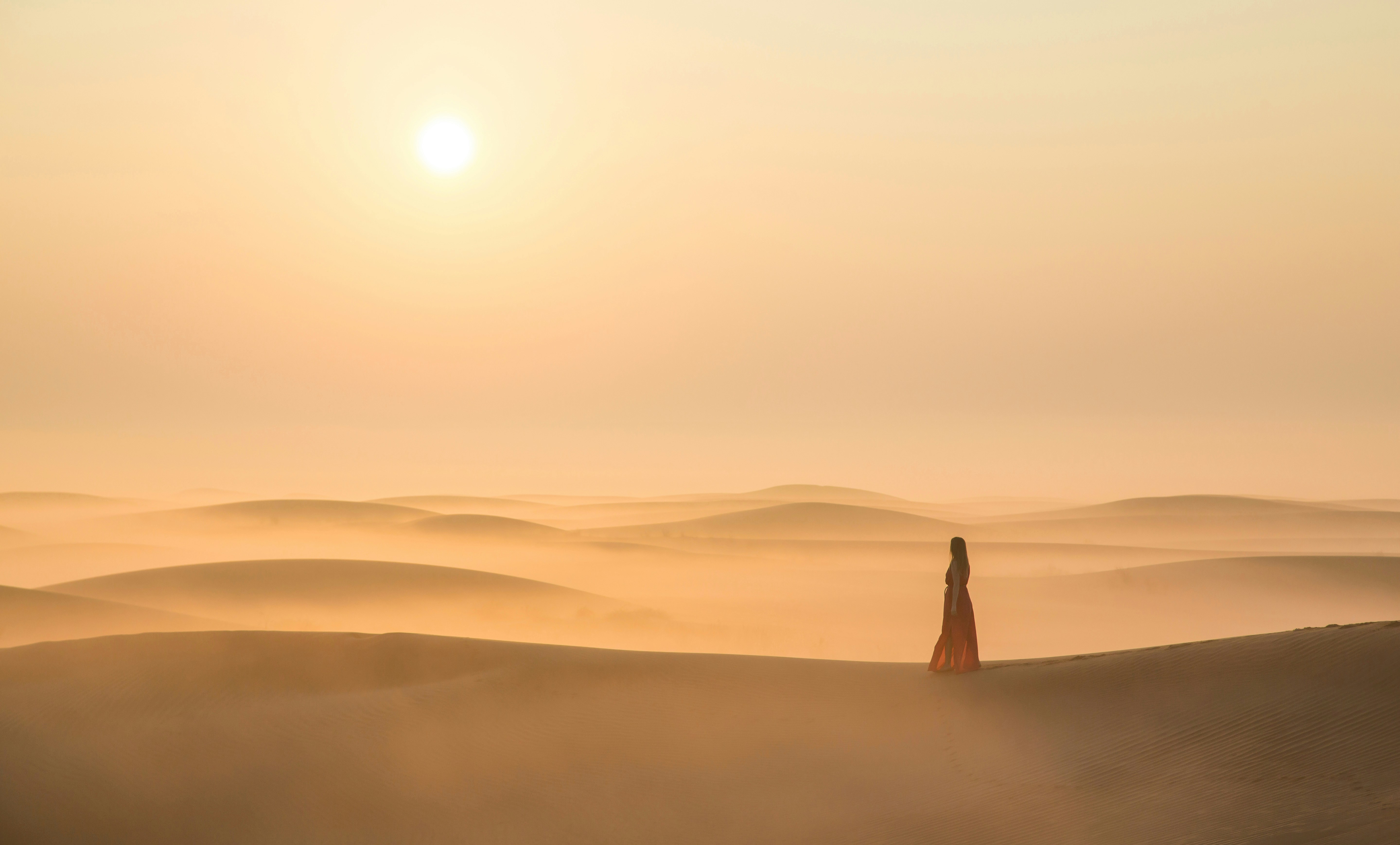 Person walking on sand dunes during sunset in Dubai desert.