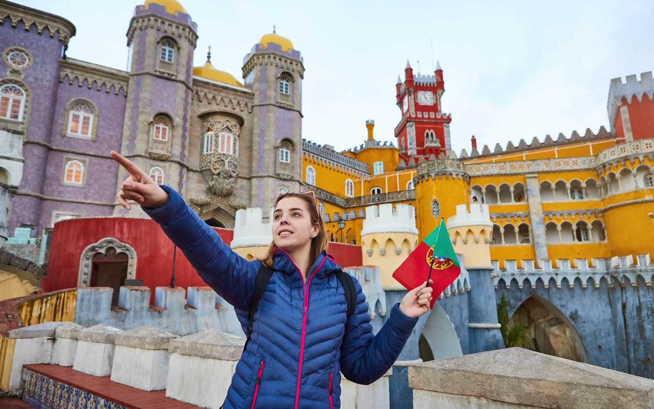 Visitor holding Portuguese flag at colorful Pena Palace, Sintra, during guided tour.