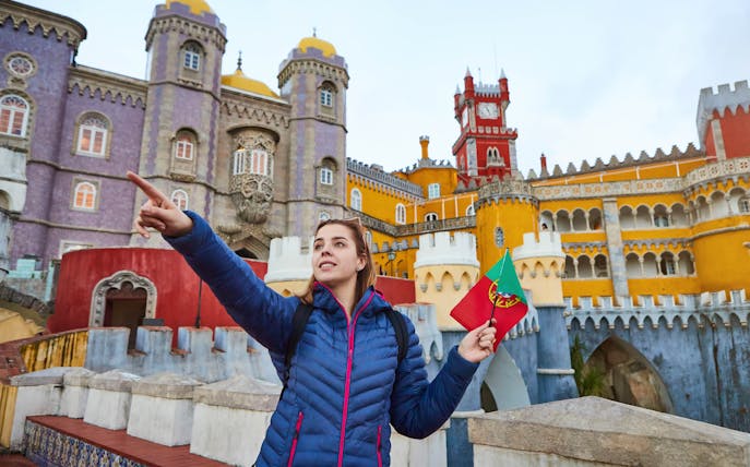 Visitor holding Portuguese flag at colorful Pena Palace, Sintra, during guided tour.