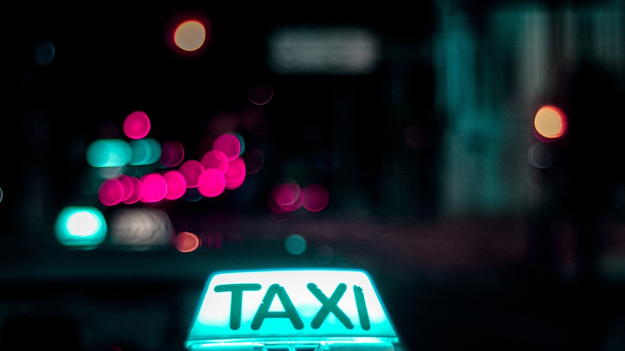 Dubai taxi sign glowing at night with blurred city lights in the background.
