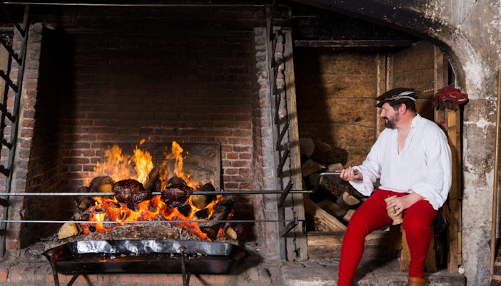 Tudor cook tending roast over open fire in Hampton Court Palace kitchen.