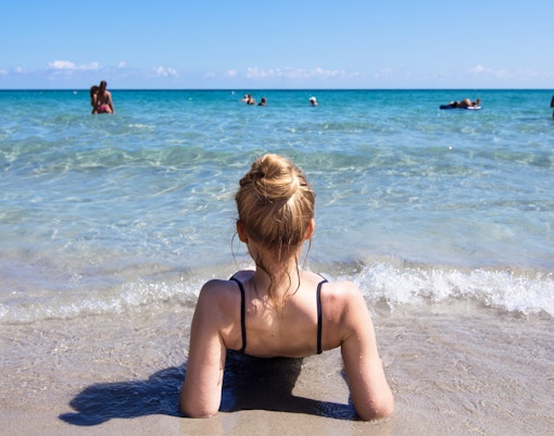 Person relaxing on a sandy beach in Italy with clear blue water.