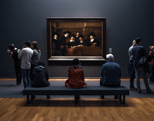 Gente mirando un cuadro en la casa museo de Rembrandt sentada en un banco