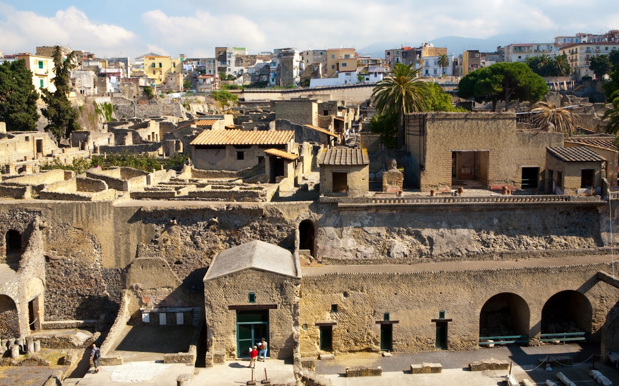 Herculaneum ruins with ancient stone buildings and modern city in the background.