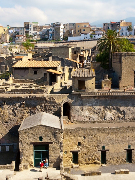 Herculaneum ruins with ancient stone buildings and modern city in the background.