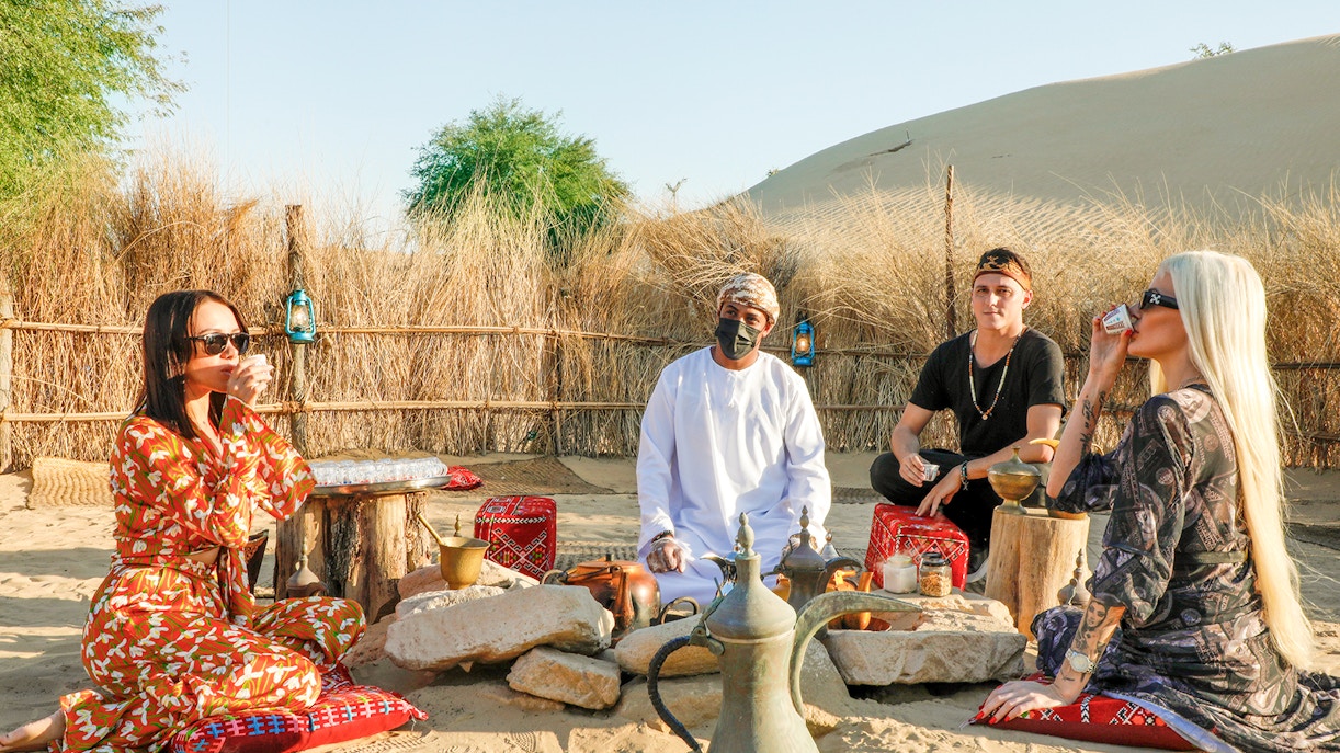 Desert camp gathering with people enjoying traditional tea in Dubai Desert, UAE.