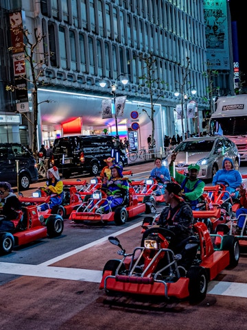 Tourists driving go-karts in Osaka dressed as Mario characters, cityscape in the background.