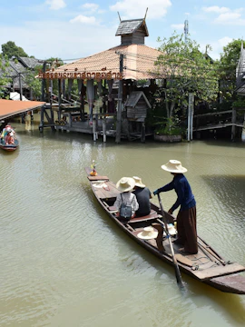 Boat navigating Pattaya Floating Market canal with traditional wooden buildings.