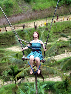 Person enjoying Bali swing over lush rice terraces.