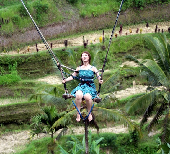 Person enjoying Bali swing over lush rice terraces.
