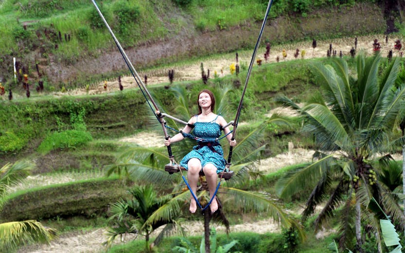 Person enjoying Bali swing over lush rice terraces.