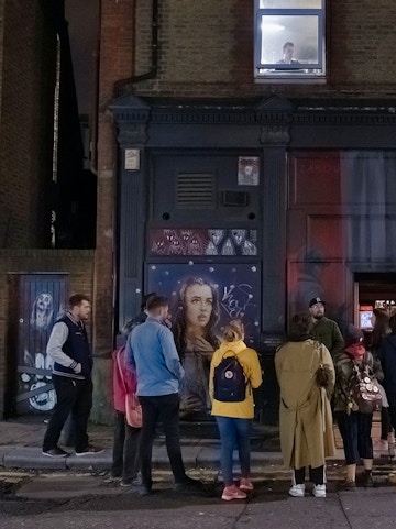 Group of people on a Jack the Ripper tour in London, standing by a mural on a brick building.