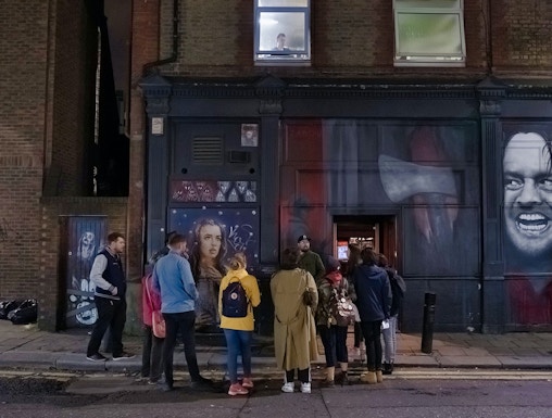 Group of people on a Jack the Ripper tour in London, standing by a mural on a brick building.