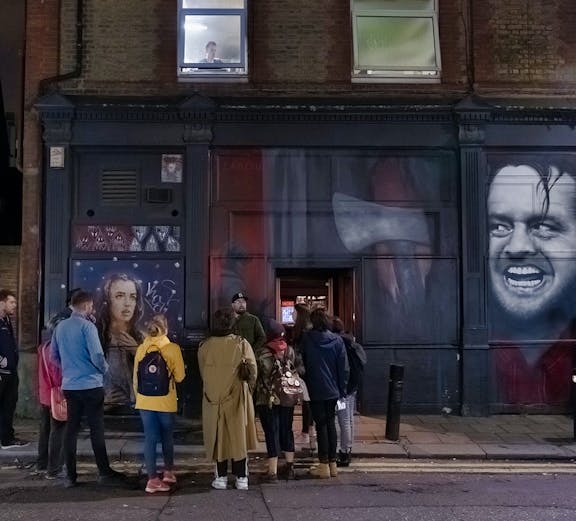 Group of people on a Jack the Ripper tour in London, standing by a mural on a brick building.