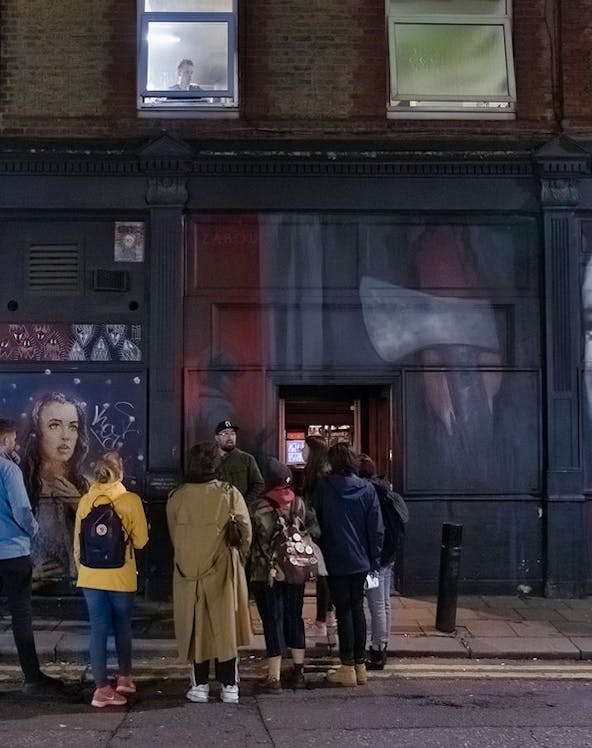 Group of people on a Jack the Ripper tour in London, standing by a mural on a brick building.