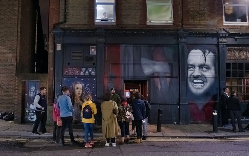 Group of people on a Jack the Ripper tour in London, standing by a mural on a brick building.