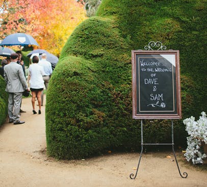 Wedding sign at Ashcombe Maze, Melbourne, with guests walking through lush greenery.