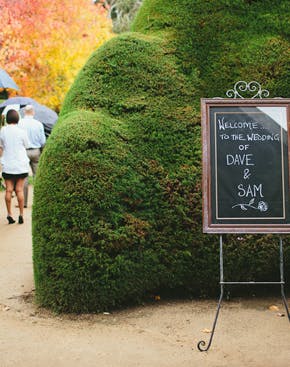 Wedding sign at Ashcombe Maze, Melbourne, with guests walking through lush greenery.