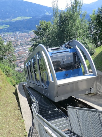 Funicular ascending a mountain in Innsbruck with city view in the background.