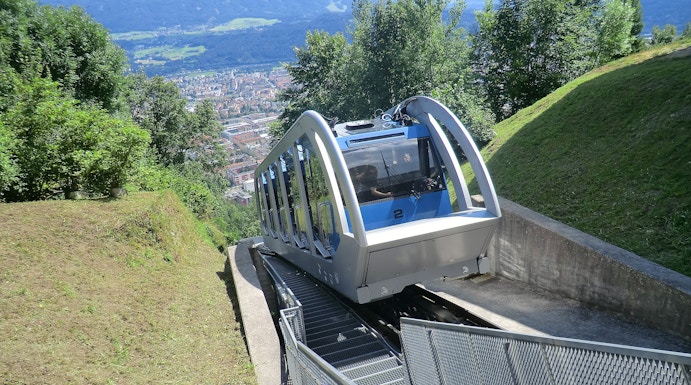 Funicular ascending a mountain in Innsbruck with city view in the background.