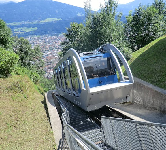 Funicular ascending a mountain in Innsbruck with city view in the background.
