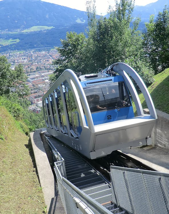 Funicular ascending a mountain in Innsbruck with city view in the background.