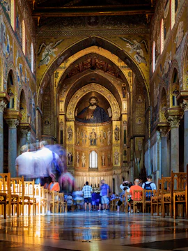 Interior of Monreale Cathedral in Palermo, featuring ornate mosaics and visitors exploring.